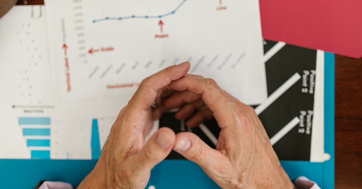 Main blanche examinant des documents financiers sur une table avec des graphiques boursiers en arrière-plan
